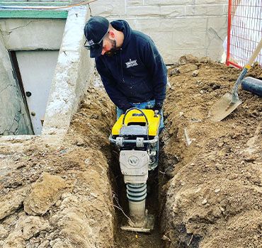 Plumber performing ground excavation for underground plumbing installation.